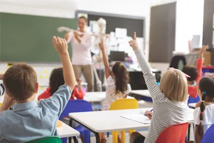 Aula di una scuola con dei bambini che alzano la mano e una maestra